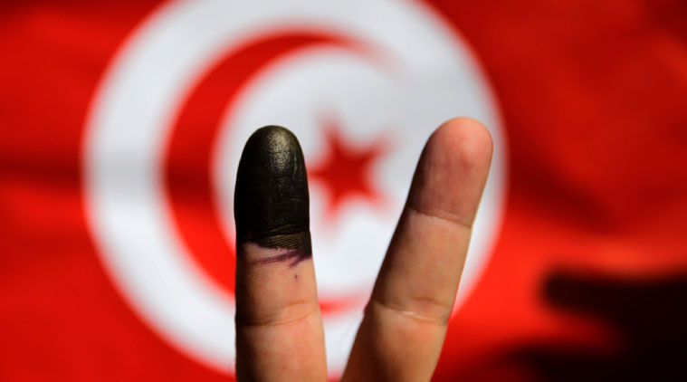 A Tunisian man shows his ink-stained finger in front of a Tunisian flag after voting for the country's parliamentary elections outside the Tunisian embassy in Cairo, Egypt, Saturday, Oct. 25, 2014. (Source: AP photo)