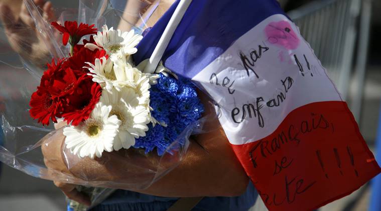 A woman carries blue, white and red flowers and a French flag as a tribute to victicms two days after an attack by the driver of a heavy truck who ran into a crowd on Bastille Day killing scores and injuring as many on the Promenade des Anglais, in Nice, France, July 16, 2016. REUTERS/Pascal Rossignol