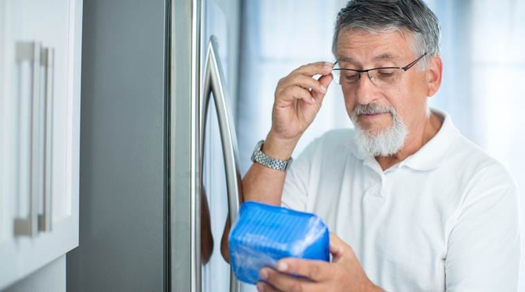 Is this still fine? Senior man in his kitchen by the fridge, looking at the expiry date of a product she took from her fridge -