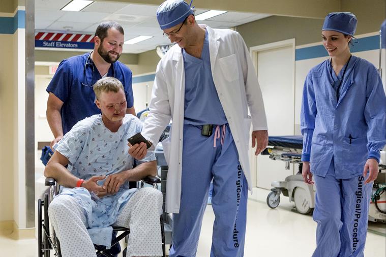 Dr Samir Mardini shows Andy Sandness photos of his children on his smartphone before Sandness' face transplant surgery. (Source: AP)