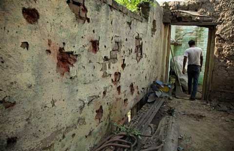 An Indian villager walks past marks on the wall of a house caused by mortar rounds fired from the Pakistan side of the border at Treva village in Arnia sector of J&K. (Source: AP)