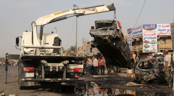 A tow truck lifts a destroyed vehicle from the site of a car bomb explosion in the largely Shiite eastern neighborhood of Talibiyah in Baghdad, Iraq, Thursday, Oct. 16, 2014. (Source: AP)