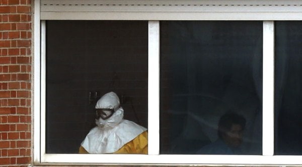 A medical practitioner wearing protective clothing stands next to an isolated patient on the sixth floor of the the Carlos III hospital in Madrid, Spain, Thursday, Oct. 9, 2014. (Source: AP)