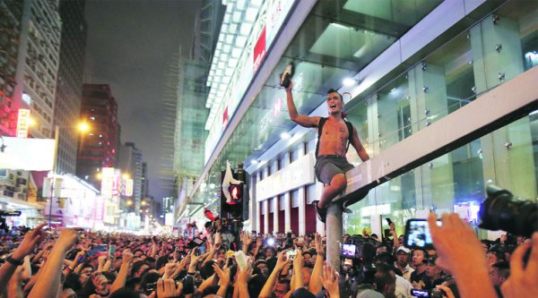 A pro-democracy student protester scales a traffic light pole in defiance to local residents in Mong Kok Friday night. (Source: AP) 