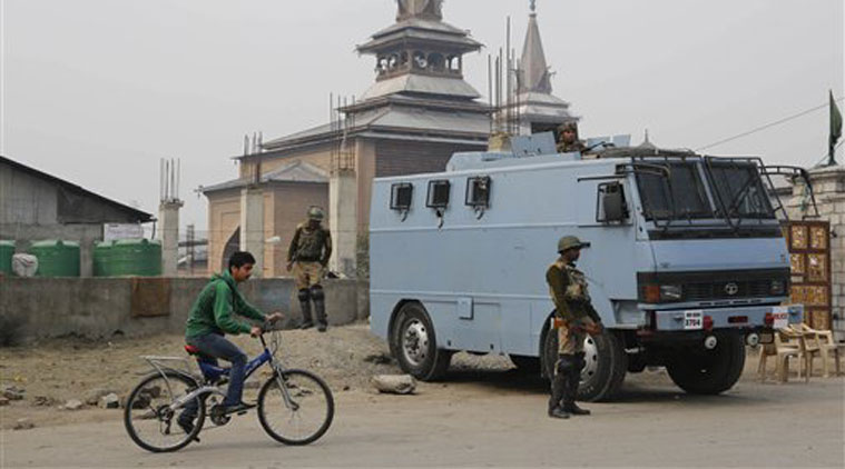A Kashmiri boy rides bicycle past Indian paramilitary soldiers keeping guard outside Jamia Masjid in Srinagar. (Source: PTI)