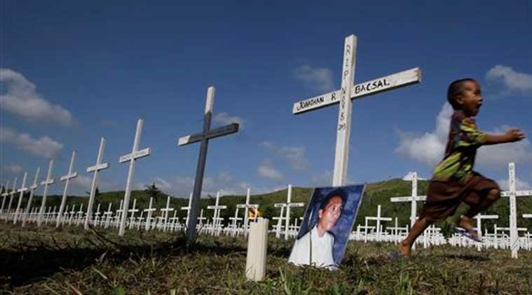 Typhoon survivor Jonathan Bacsal Jr., runs past a cross that indicates his father Jonathan Bacsal Sr. is buried at a mass grave for typhoon Haiyan victims (Source: AP)