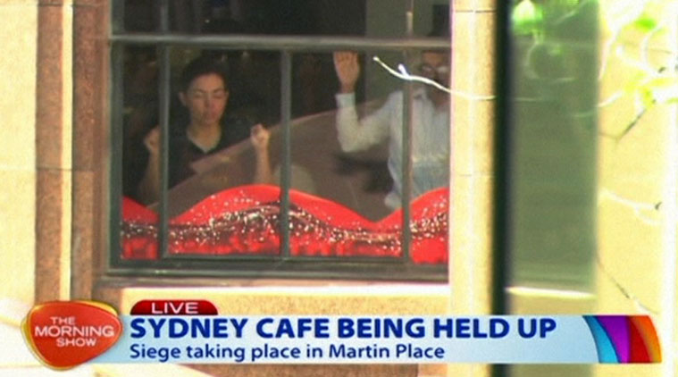 This image taken from video shows people holding up hands inside a cafe in Sydney, Australia Monday, Dec. 15, 2014. An apparent hostage situation was unfolding inside the chocolate shop and cafe in Australia's largest city on Monday, where several people could be seen through a window with their hands held in the air. (AP Photo/Channel 7 vide AP Video) 