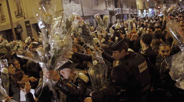 People hold bouquet of flowers as a French police officer tries to maintain the mob during a demonstration outside a kosher grocery store where four hostages were killed on Friday in Paris, Saturday, Jan. 10, 2015. Hundreds of thousands of people marched Saturday in cities from Toulouse in the south to Rennes in the west to honor the victims, and Paris expects hundreds of thousands more at Sunday’s unity rally. (AP Photo/Francois Mori)
