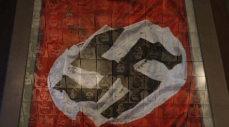 In this photo taken Saturday, March 21, 2015, a Nazi flag is displayed at the Holocaust Museum in the town of Kalavryta, western Greece, as portraits of victims are reflected in a glass pane. It was 1943 and the Nazis were deporting Greece's Jews to death camps in Poland. Hitler's genocidal accountants reserved a chilling twist: The Jews had to pay their train fare. The bill for 58,585 Jews sent to Auschwitz and other camps exceeded 2 million Reichsmark — more than 25 million euros ($27 million) in today's money. For decades, this was a forgotten footnote among all of the greater horrors of the Holocaust. Today it is returning to the fore amid the increasingly bitter row between Athens and Berlin over the Greek financial bailout. (AP Photo/Petros Giannakouris)