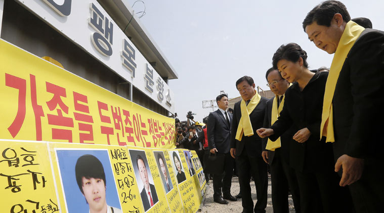 South Korean President Park Geun-hye, second from right, looks at portraits of the victims of the sunken ferry Sewol as she arrives to offer her condolences to the bereaved relatives of the victims at a port in Jindo, South Korea, Thursday, April 16, 2015. Tears and grief mixed with raw anger Thursday as black-clad relatives mourned more than 300 people, mostly high school kids, killed one year ago when the ferry Sewol sank in cold waters off the southwestern South Korean coast. The letter a banner at center read " We denounced the government". (Lee Jeong-ryong/Yonhap via AP) 