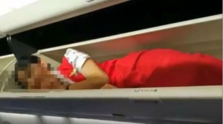 Image which shows female cabin crew lying in overhead luggage compartment/ Screenshot