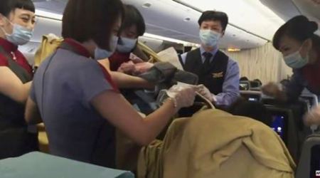In an image from AP video, a member of the plane's crew holds up a newborn after Dr. Angelica Zen, who is obscured at lower right, delivered the baby on a China Air flight from Taiwan on Oct. 7, 2015. A passenger had gone into labor, and the flight was diverted to Alaska. Mother and newborn daughter left for a hospital, and the flight continued on to Los Angeles. (Edmund Chen/AP Video via AP Photo)