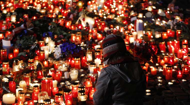 A young girl sits next to flowers and candles placed outside the French embassy in Prague. (Source: AP)