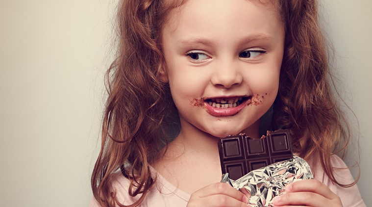 Curious cute kid girl eating dark chocolate and looking fun