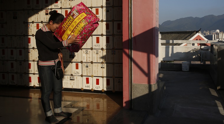 In this Nov. 28 photo, a woman prays as she holds a package of paper money intended to be burned as offerings to her dead father with a wall of niches for cremated remains in the background at a private columbarium in Hong Kong. In tightly-packed Hong Kong, the dead are causing a problem for the living. (AP Photo/Kin Cheung)