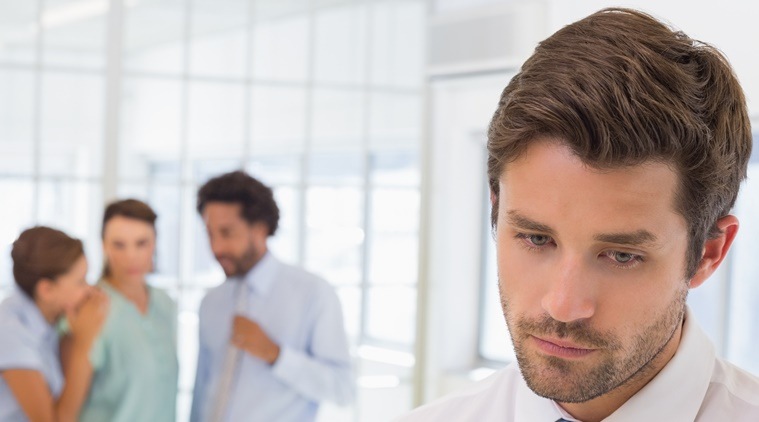 Colleagues gossiping with sad businessman in foreground