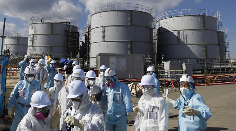Members of a media tour group wearing a protective suit and a mask walk together after they receive a briefing from Tokyo Electric Power Co. (TEPCO) employees (in blue) in front of storage tanks for radioactive water at the tsunami-crippled Fukushima Dai-ichi nuclear power plant in Okuma.