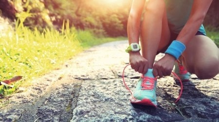 young woman runner tying shoelaces on stone trail
