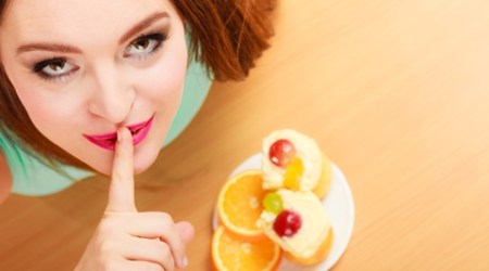 Woman eating cake showing quiet sign. Gluttony.