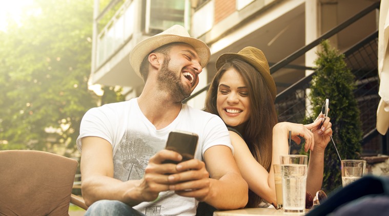 Photo of a happy couple laughing while looking at mobile phone
