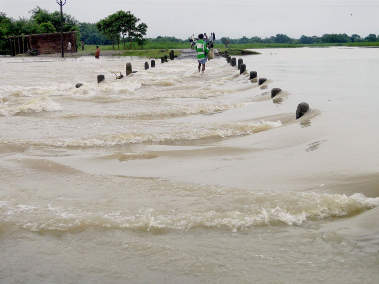 People walk through a submerged a bridge in a flood-hit village in Kishanganj district of Bihar on Wednesday. (Source: PTI)