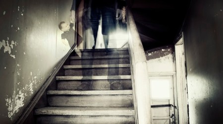 Ghostly figure standing on stairs inside a hounted house holding doll