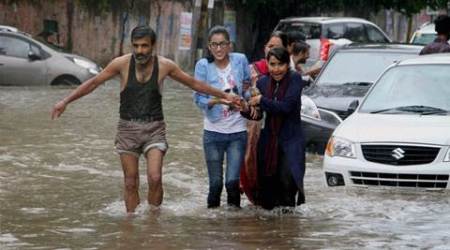 Jammu: A man helps girls move through a flooded street during heavy rains in Jammu on Sunday. PTI Photo  (PTI8_7_2016_000086A)