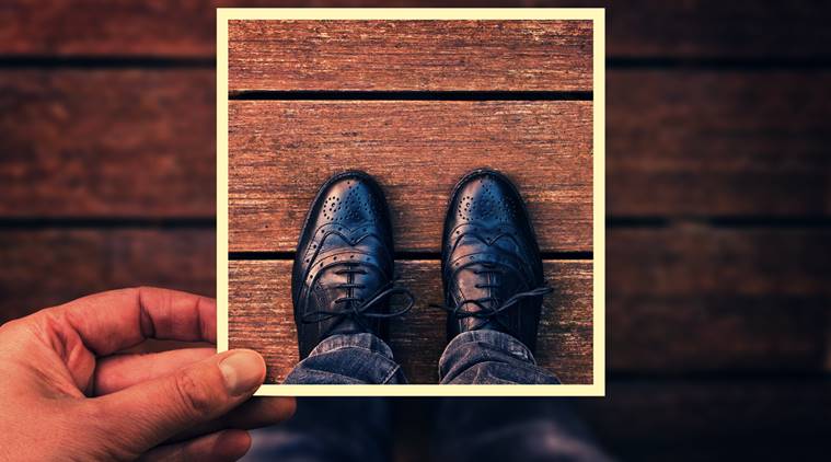 Selfie of foot and legs with black derby shoes seen from above with hand holding an instant photo frame, vintage process