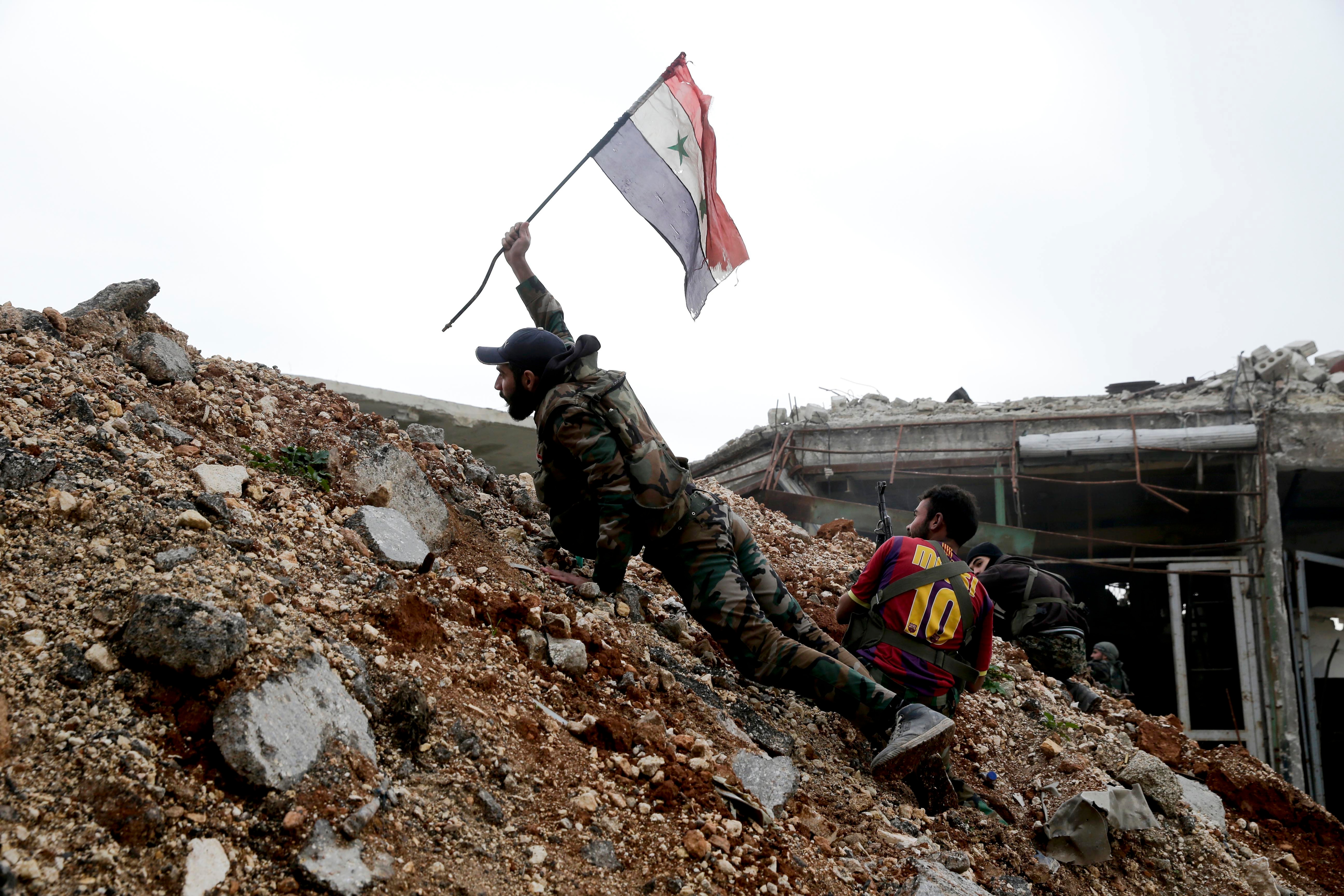 A Syrian army soldier places a Syrian national flag during a battle with rebel fighters at the Ramouseh front line, east of Aleppo, Syria, Monday, Dec. 5, 2016. (AP Photo/Hassan Ammar, File)