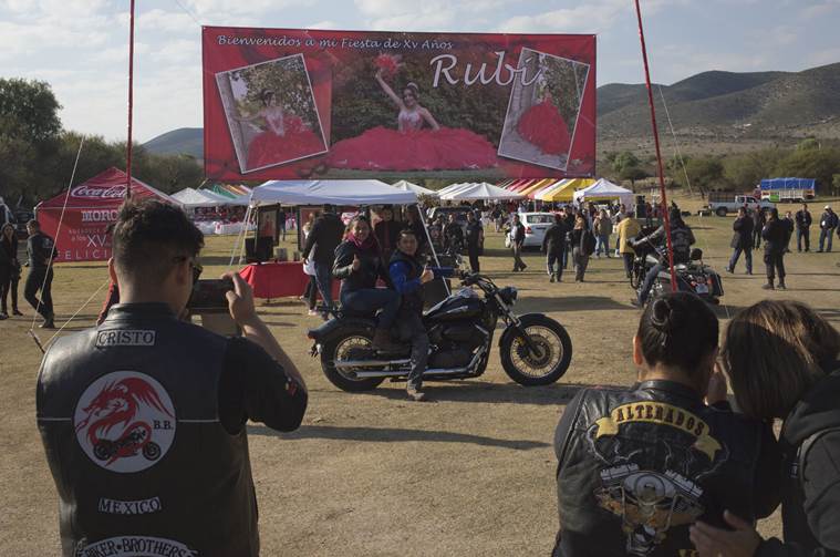 A couple, who traveled from Mexico City with a group of bikers, pose for a photo backdropped by a banner welcoming visitors to Rubi Ibarra's down-home 15th birthday party in the village of La Joya, San Luis Potosi State, Mexico (AP Photo/Enric Marti)
