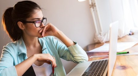 Young female blogger working at home.She sitting in her working room and typing something on laptop.Startup business.Looking worried.