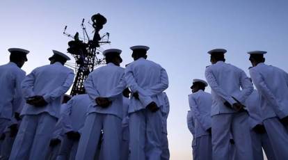 An Indian Navy sailor adjusts his colleague's uniform prior to the