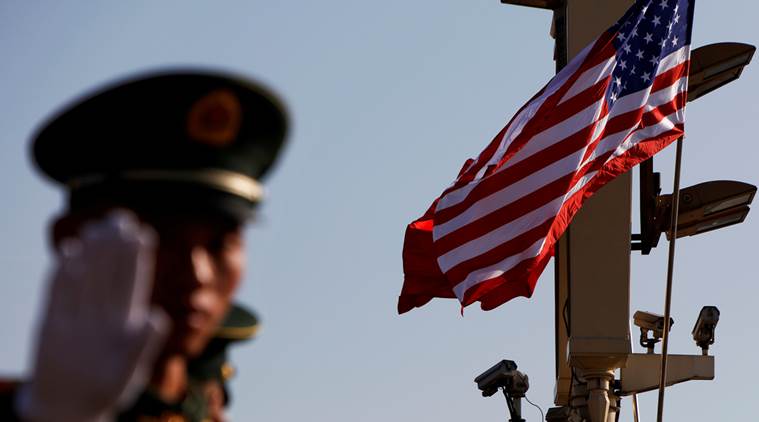 A paramilitary policeman gestures under a pole with security cameras, U.S. and China's flags.