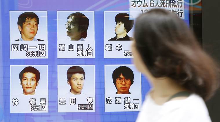 A woman walks on a street while watching TV news reporting executions of six members of Aum Shinrikyo, in Tokyo.
