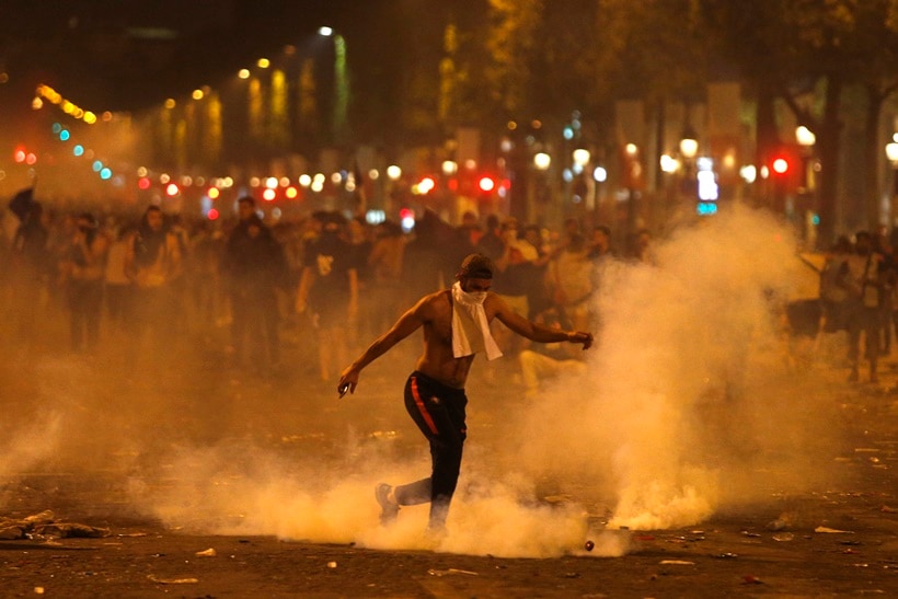 A man kicks a tear gas canister thrown by riot police during clashes on the Champs Champs Elysees avenue where soccer fans were celebrating France's World Cup victory over Croatia in Paris