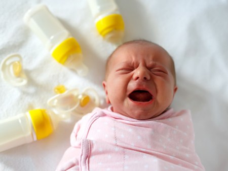Crying newborn baby girl with nursing bottles. Formula drink for babies.