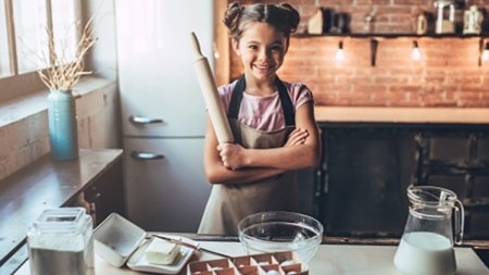 Little cute girl is cooking on kitchen. Having fun while making cakes and cookies. Smiling and looking at camera.