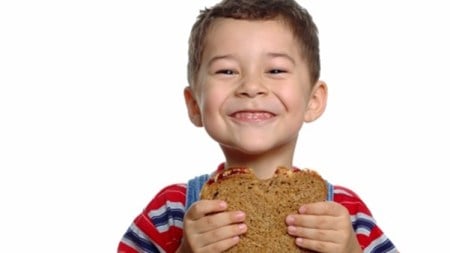 A 5-year-old boy enjoying a peanut butter and jelly sandwich on whole wheat bread