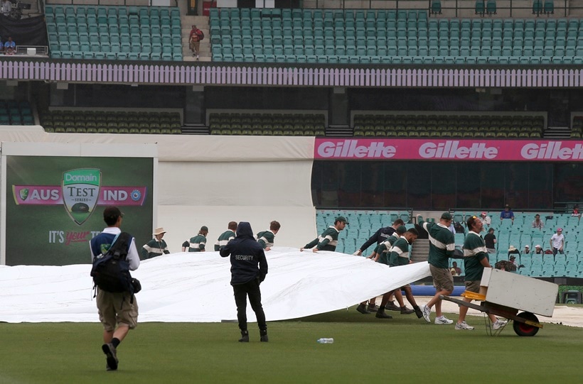 Grounds crew pull a tarpaulin over the pitch as rain falls during a delay before play on day 5 of the cricket test match between India and Australia in Sydney