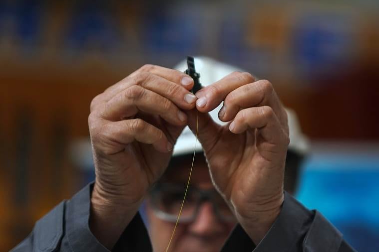 A worker holds a glass strand that will be woven into a fiber-optic cable