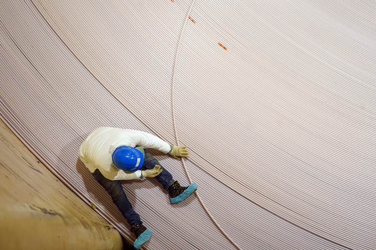 A worker sits on a giant spool of fiber-optic cable