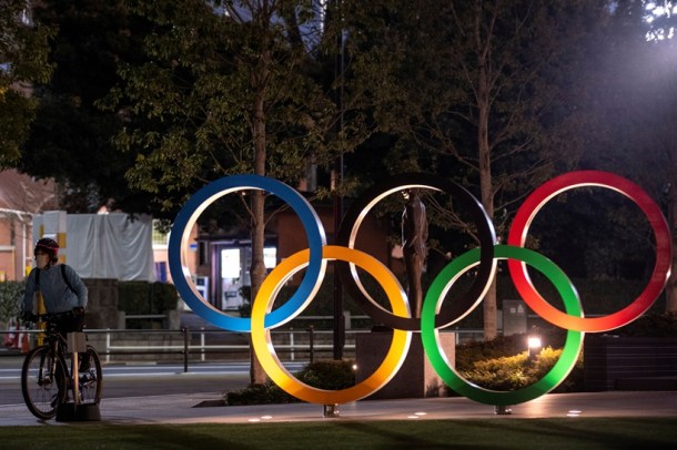 A woman wearing a protective face mask, following the outbreak of the coronavirus, rides her bicycle past The Olympic rings in front of the Japan Olympics Museum in Tokyo