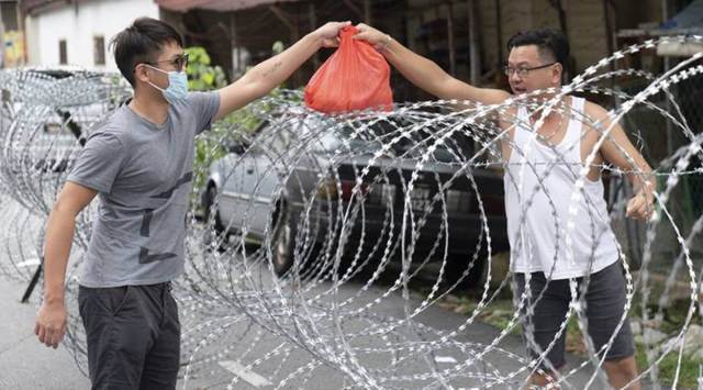 A man collect supplies over barbed wire in the coronavirus locked down area of Selayang Baru, outside of Kuala Lumpur, Malaysia, Sunday, April 26, 2020. The lockdown was implemented to allow authorities to carry out screenings to help curb the spread of coronavirus. (AP Photo/Vincent Thian)