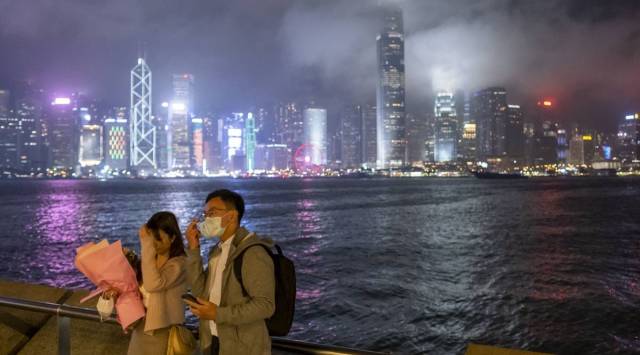 People adjust their hair and a protective mask while posing for a selfie photograph against the city skyline at night in the Tsim Sha Tsui district of Hong Kong, China (Blooomberg)