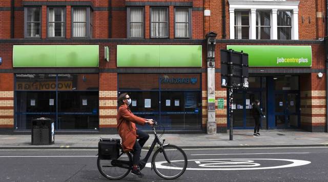 A woman wearing a mask to protect against coronavirus, rides a bicycle past a job centre in Shepherd's Bush, as the lockdown to curb the spread of coronavirus continues, in London. (AP Photo/Alberto Pezzali, File)