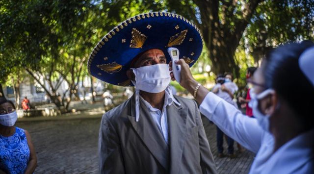 A nurse measures the temperature of a mourner wearing a Mexican hat, and a protective face mask as a precaution against the spread of the new coronavirus.(AP Photo/Ramon Espinosa)