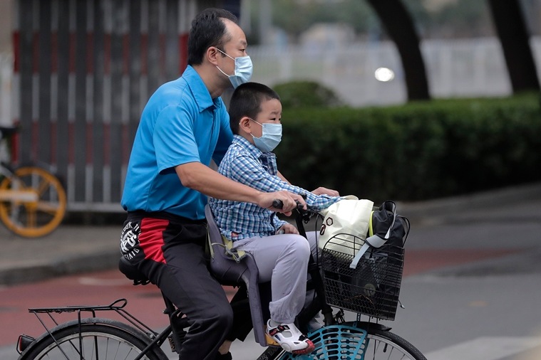 A man and a child wearing face masks to help curb the spread of the coronavirus ride on a bicycle past a street in Beijing. (File photo via AP)