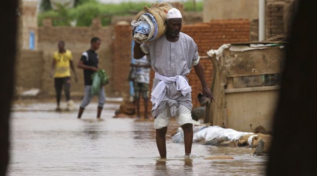 A man carries belongings as he wades through of a flooded road in the town of Shaqilab, about (25 km) southwest of the capital, Khartoum, Sudan. (AP Photo/File)