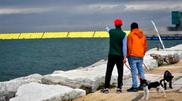 People look at yellow barriers being raised during high water in Venice, northern Italy, Saturday, Oct. 3, 2020. Controversial and long-delayed underwater barriers passed their first emergency with flying colors on Saturday, protecting the Italian lagoon city of Venice from a tide that peaked at 130 centimeters (51-inches), a level that would normally inundate about half of the city.  (Claudio Furlan/LaPresse via AP)