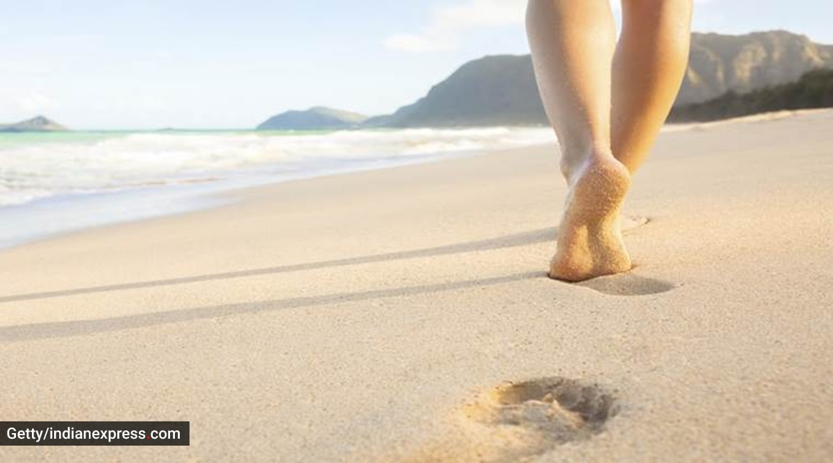  A person walking barefoot on a beach, leaving footprints in the sand.